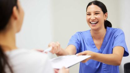 Eine Pflegerin reicht lächelnd einem Patienten ein Formular und einem Stift